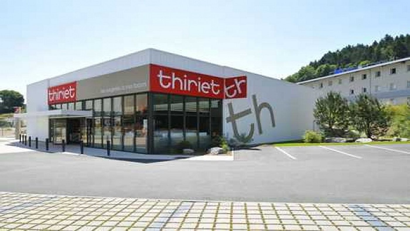 Façade moderne d’un magasin Thiriet aux enseignes rouges et blanches, avec grandes vitres et parking vide au premier plan.